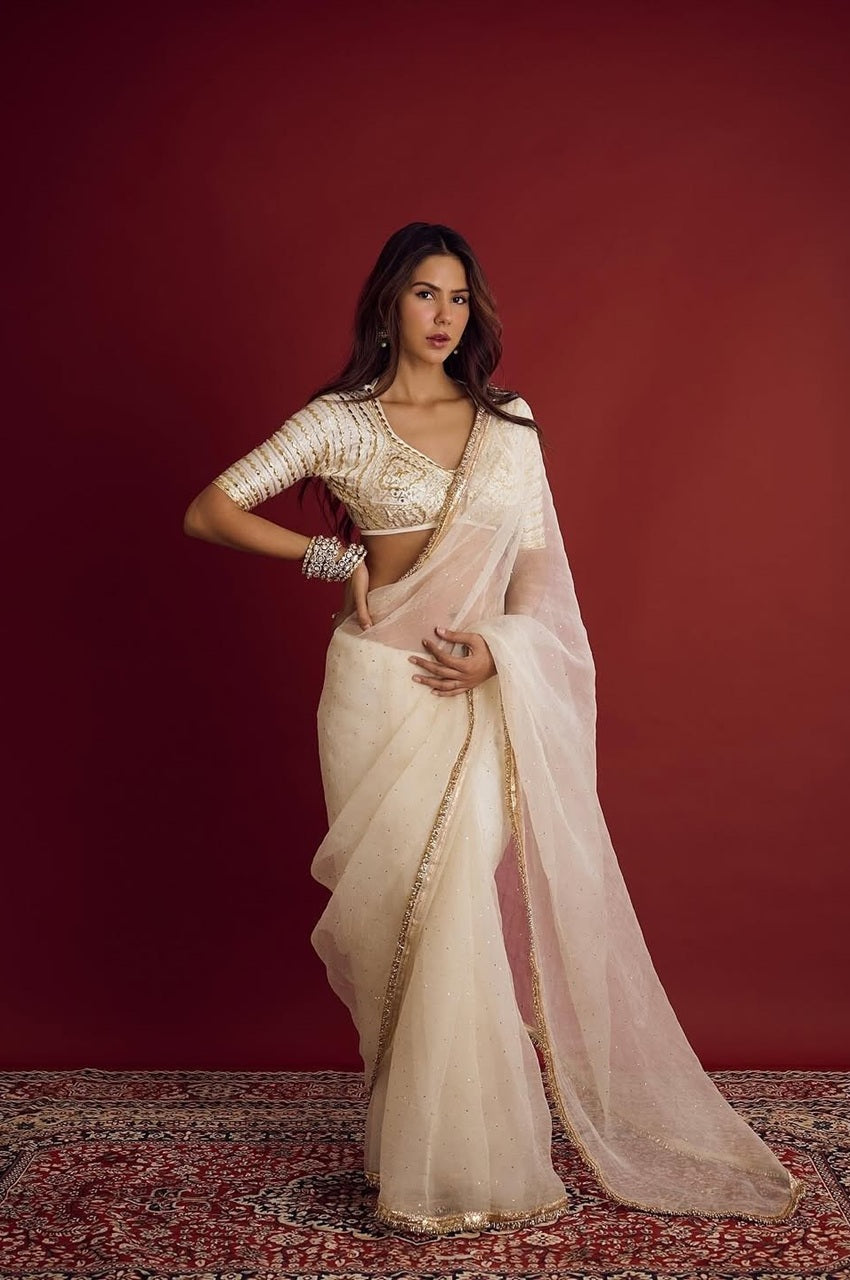 Woman in a white saree with gold details against a red background